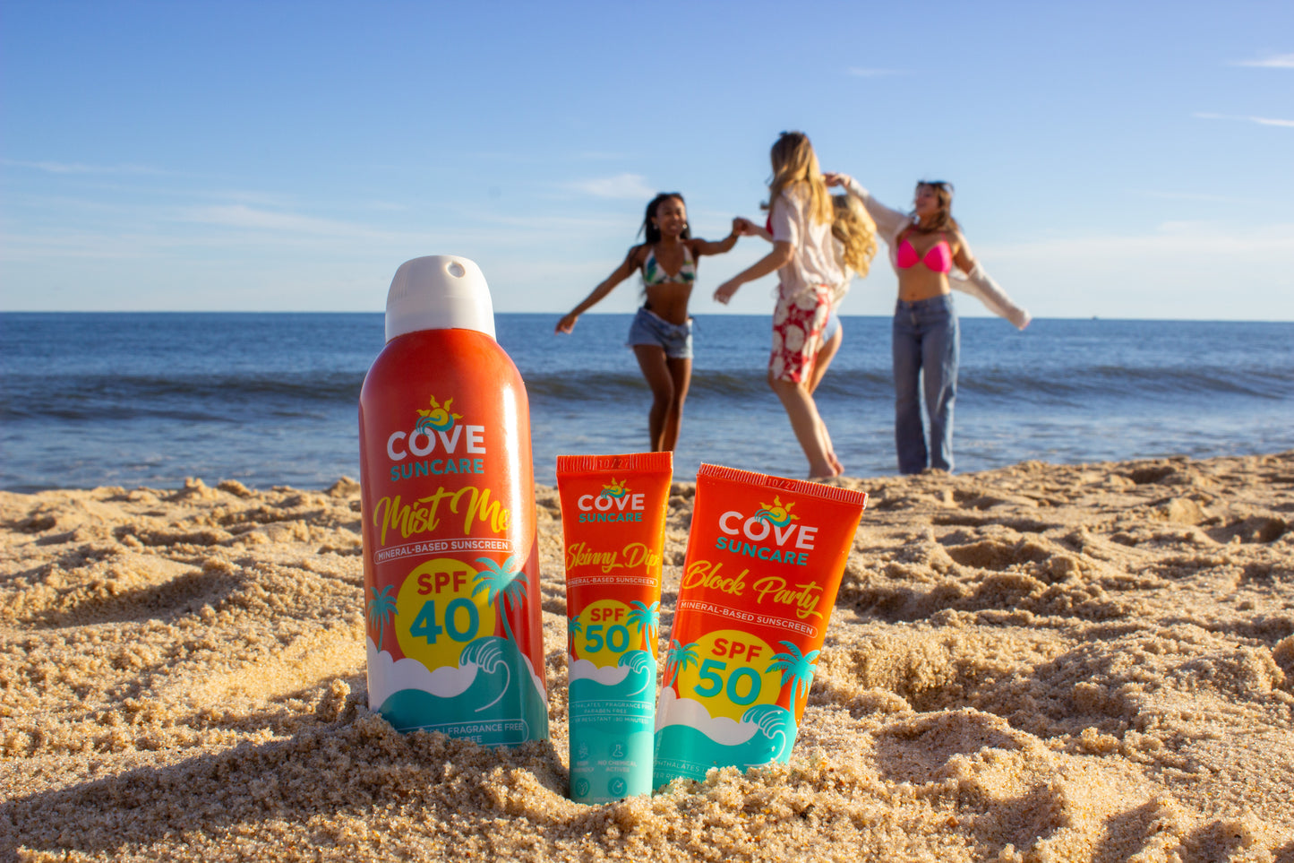 Cove sunscreen bottles labeled SPF 40 and 50 stand on a sandy beach.