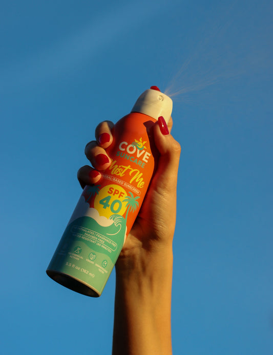 A hand holding sunscreen spray labeled "Cove Suncare, SPF 40.