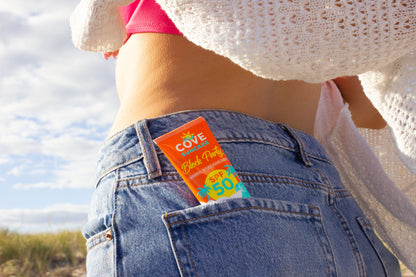 A person in jeans stands with sunscreen labeled "Cove, SPF 50" in their pocket.