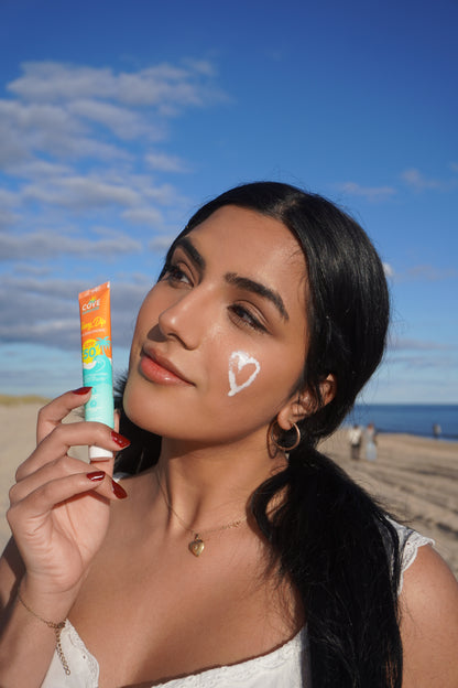 A woman at the beach holds cove sunscreen tube against the blue sky.